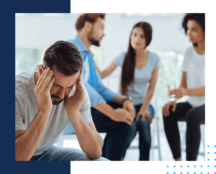 A group of people sitting around and one man is looking sad.