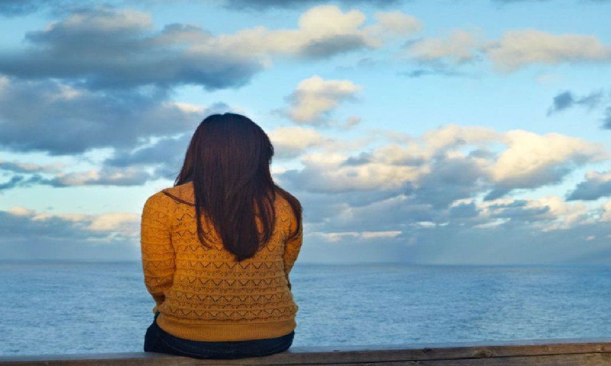 A woman sitting on the edge of a pier looking out at the ocean.