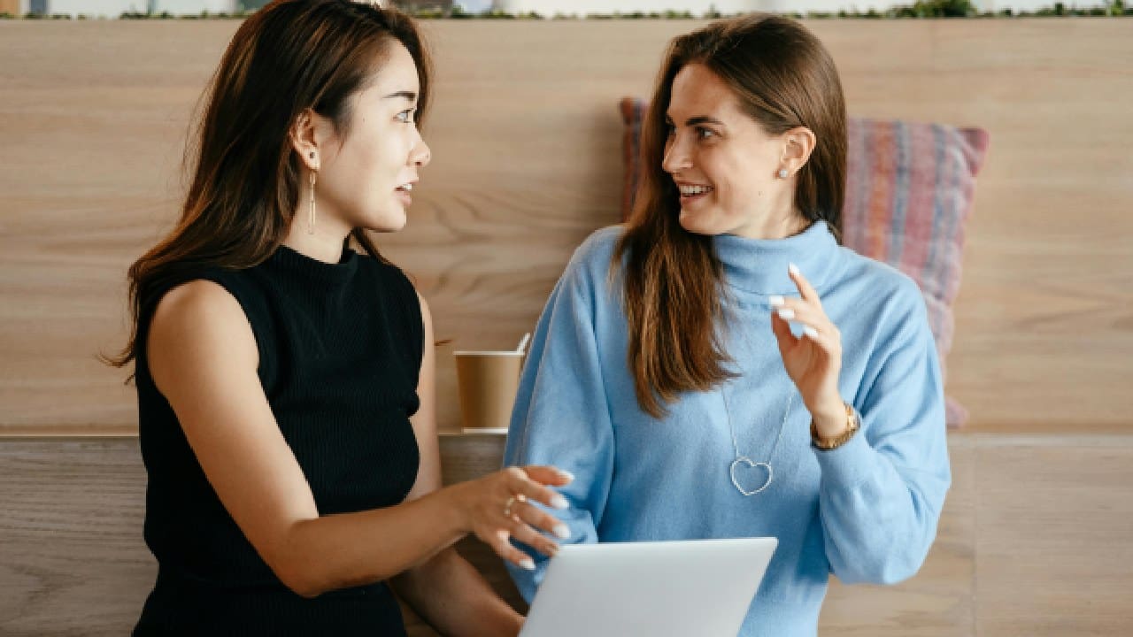 Two women are talking to each other while holding a laptop.