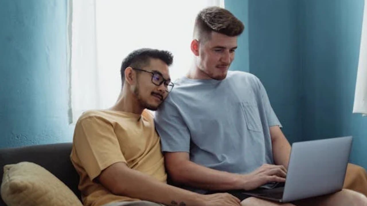 Two men sitting on a couch looking at a laptop.