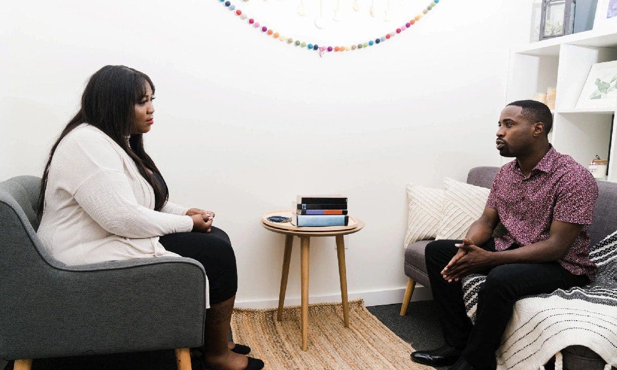 Two people sitting in a room with one of them talking to another person.