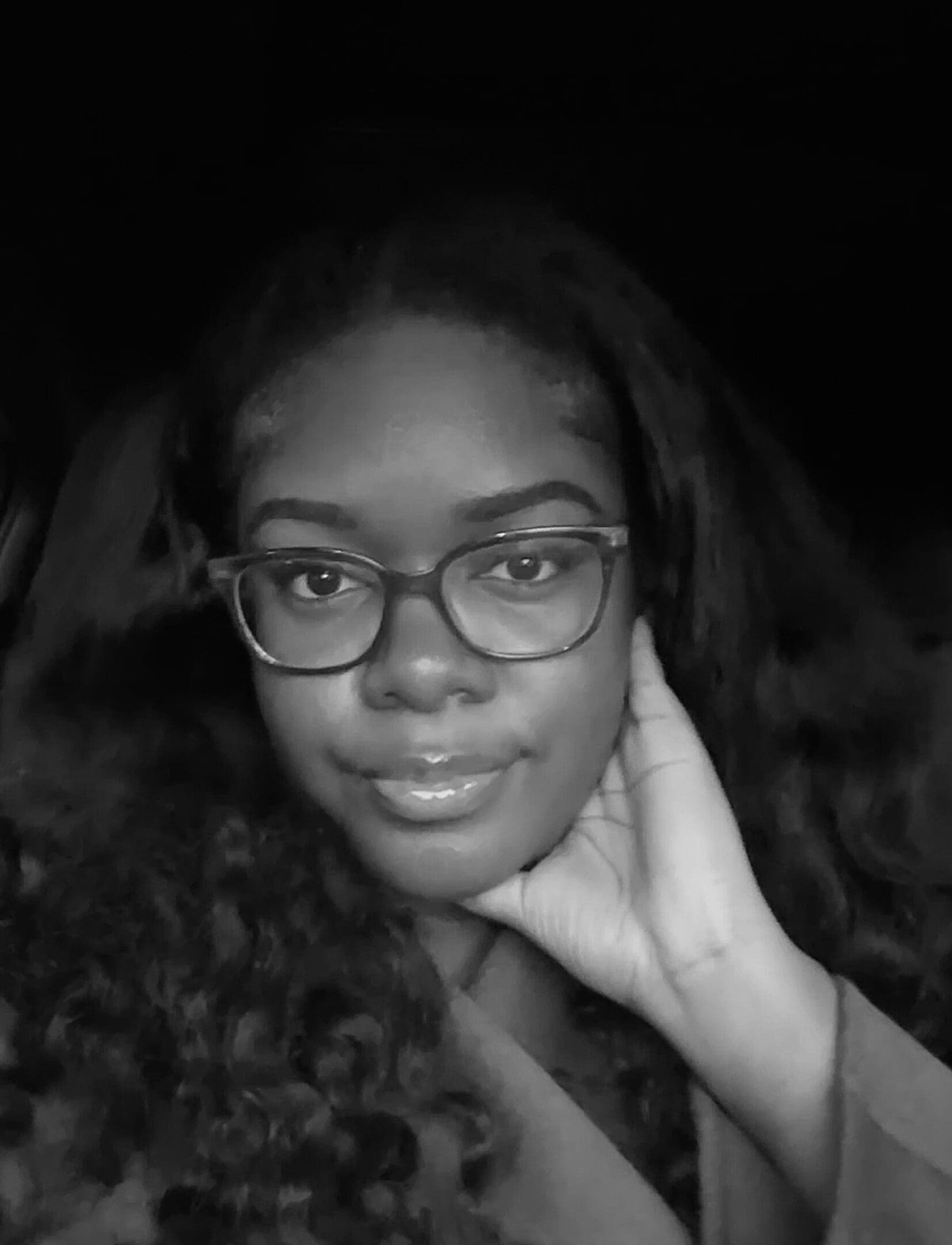 Woman with glasses, hand on face, smiling.