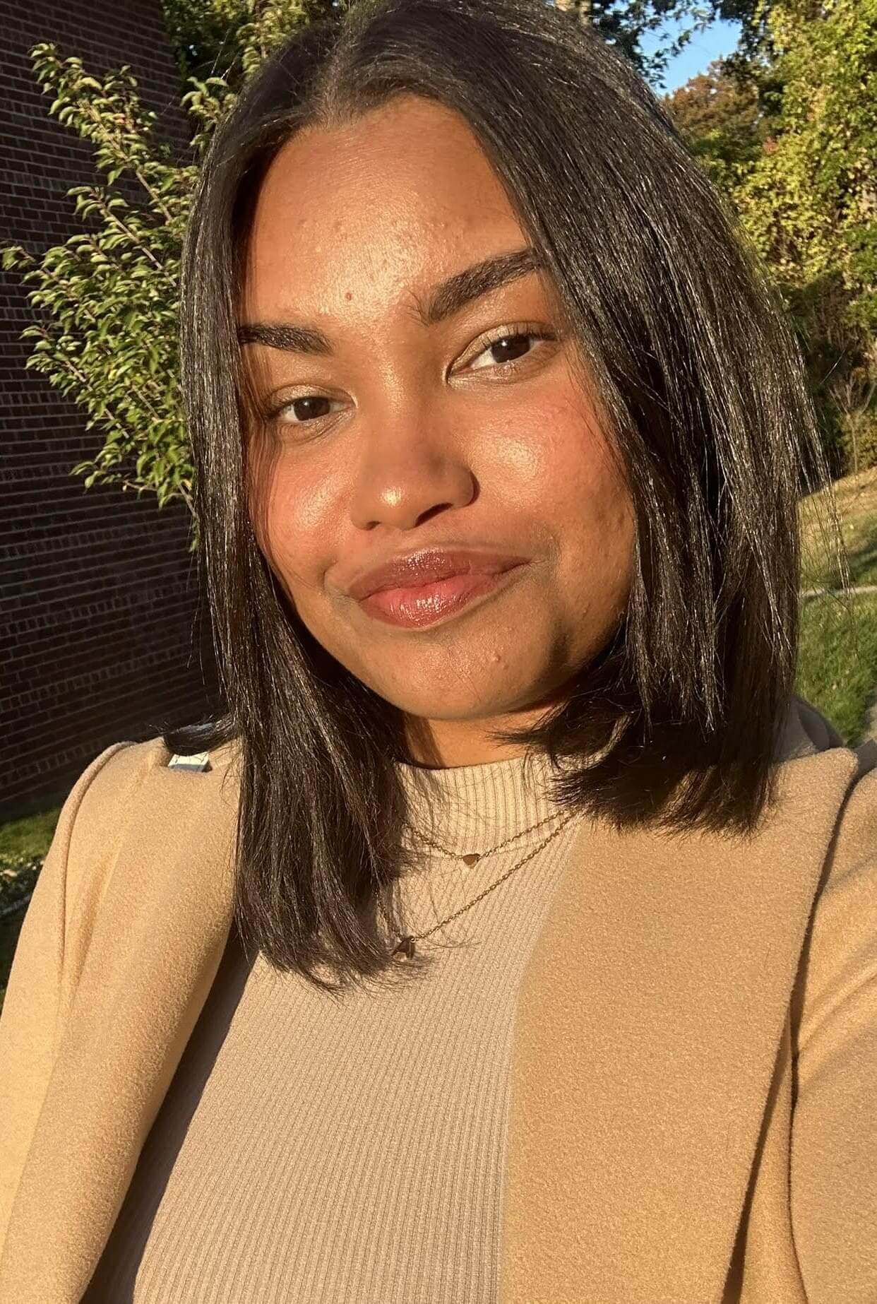 Woman smiling outdoors in sunlight.